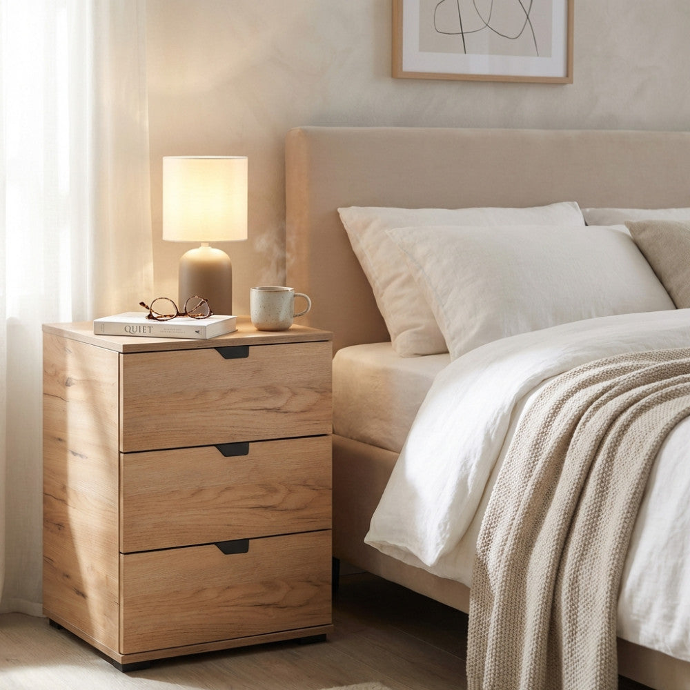 Comodino Duero in rovere chiaro ambientato in una camera da letto luminosa con lampada accesa.