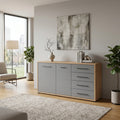 Credenza Lisabon in rovere artigiano e grigio grafite ambientata in un living luminoso con piante decorative.