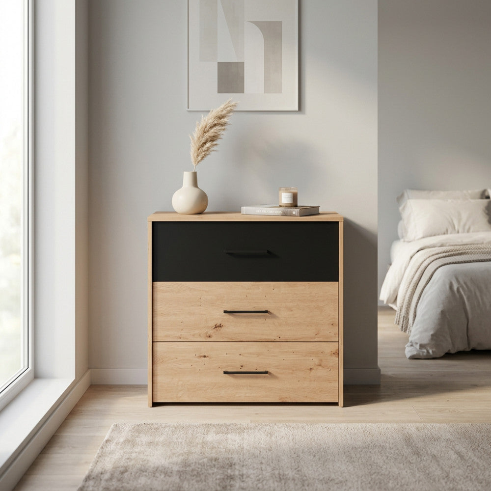 Comò Varadero in rovere chiaro con cassetto superiore nero opaco, ambientato in una camera da letto luminosa e moderna.