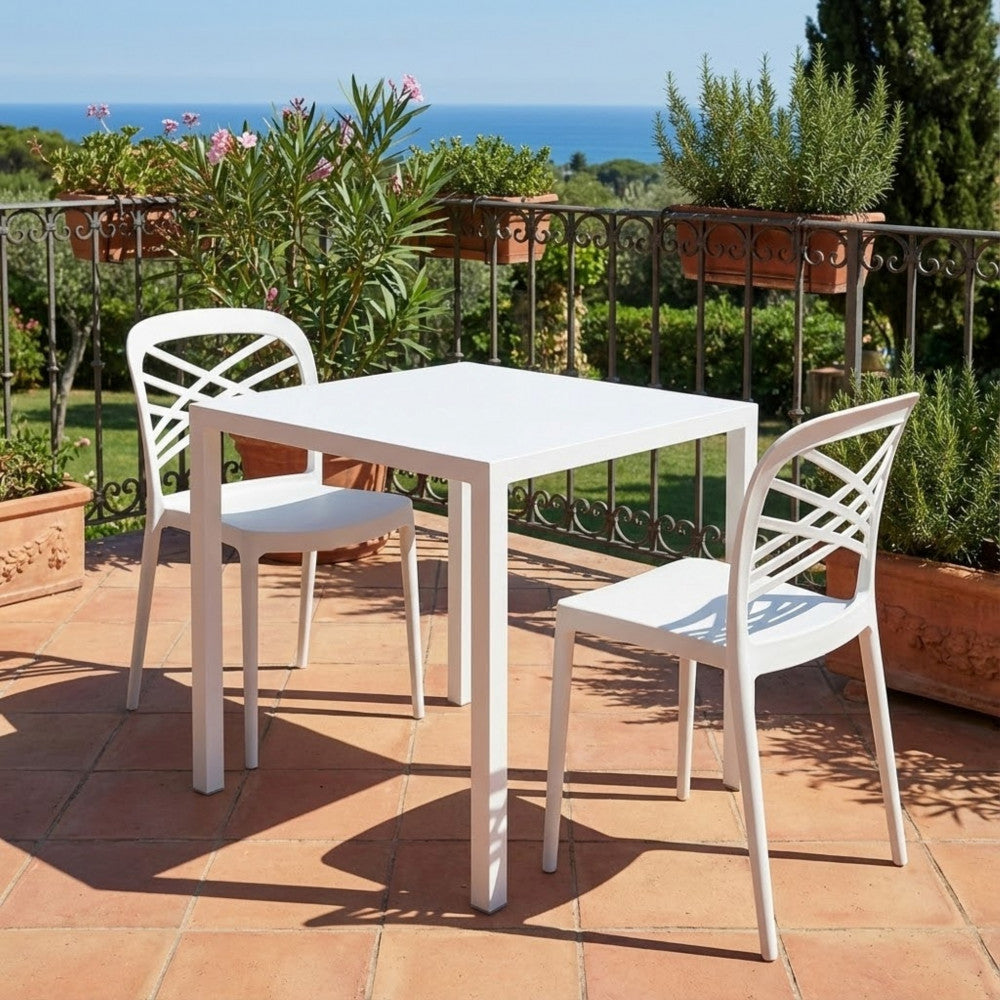Tavolo da giardino in acciaio bianco abbinato a due sedie coordinate su una terrazza in cotto con vista mare.