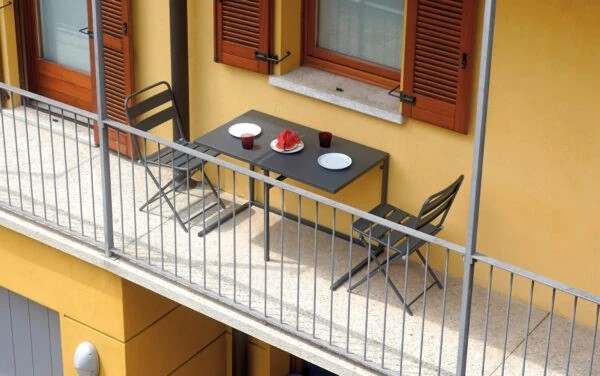 Panoramica Set completo per balcone pieghevole BSF04 con tavolo 100x50 cm e due sedie, realizzato in ferro robusto, su un balcone arredato | Albert Stock