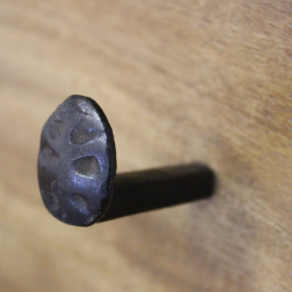 Macro dettaglio del gancio in metallo forgiato inserito nel pannello di legno massello.