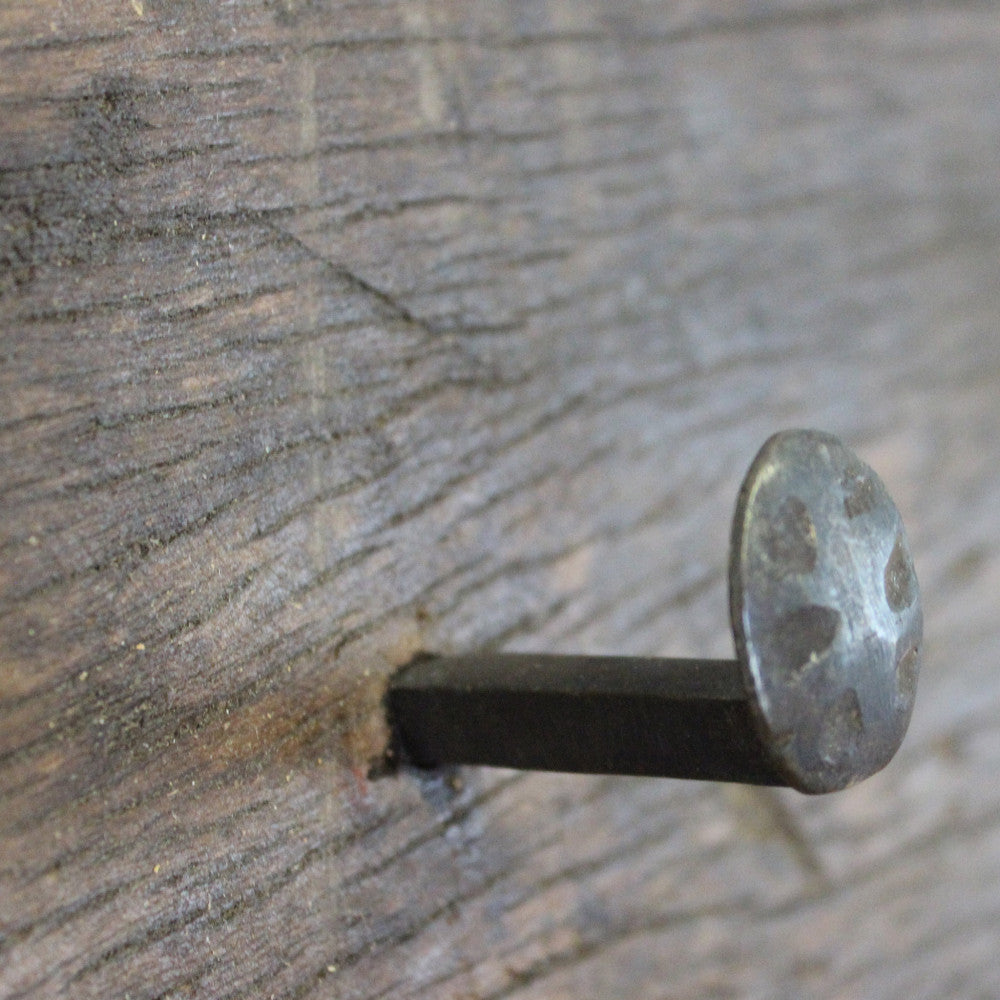 Dettaglio macro della testa del chiodo in metallo forgiato incastonata nel legno riciclato di prima qualità dell'appendiabiti Frederick.
