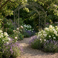 Arco da giardino Anderson in acciaio bianco ossidato, posizionato su un sentiero in ghiaia circondato da lavanda e ortensie.