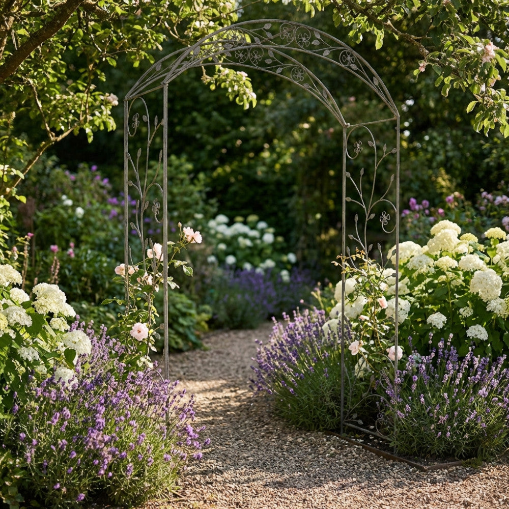 Arco da giardino Anderson in acciaio bianco ossidato, posizionato su un sentiero in ghiaia circondato da lavanda e ortensie.