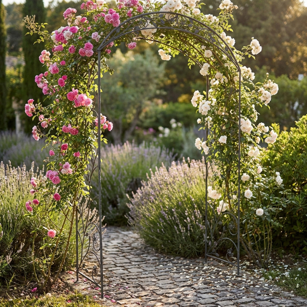 Arco in acciaio bianco ossidato completamente avvolto da rose rampicanti rosa e bianche su un percorso in pietra.