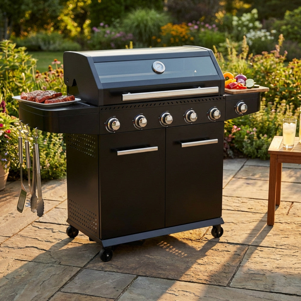 Dettaglio laterale del barbecue Maine in metallo nero, posizionato su pavimentazione in pietra con carne in cottura.