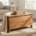 Baule Carlyle in legno massello marrone ambientato in un luminoso soggiorno, utilizzato come tavolino con libri e una tazza.
