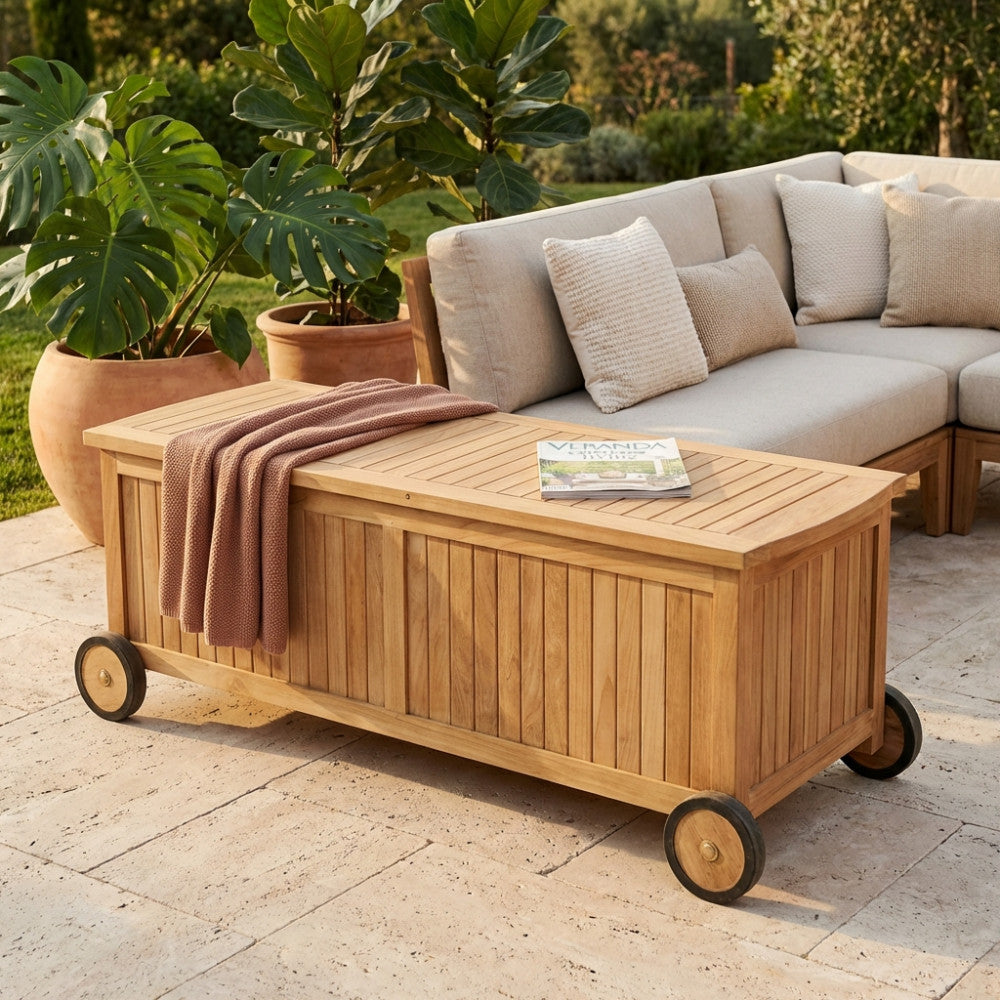 Contenitore in teak BOX NAGOYA affiancato a un divano outdoor, con una coperta e una rivista appoggiate sopra.