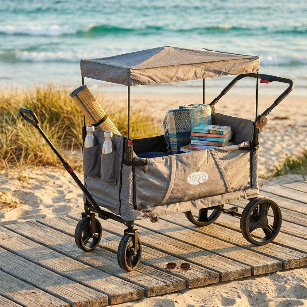 Carrello da esterno in metallo e poliestere con tettuccio, contenente libri e coperte su una spiaggia.