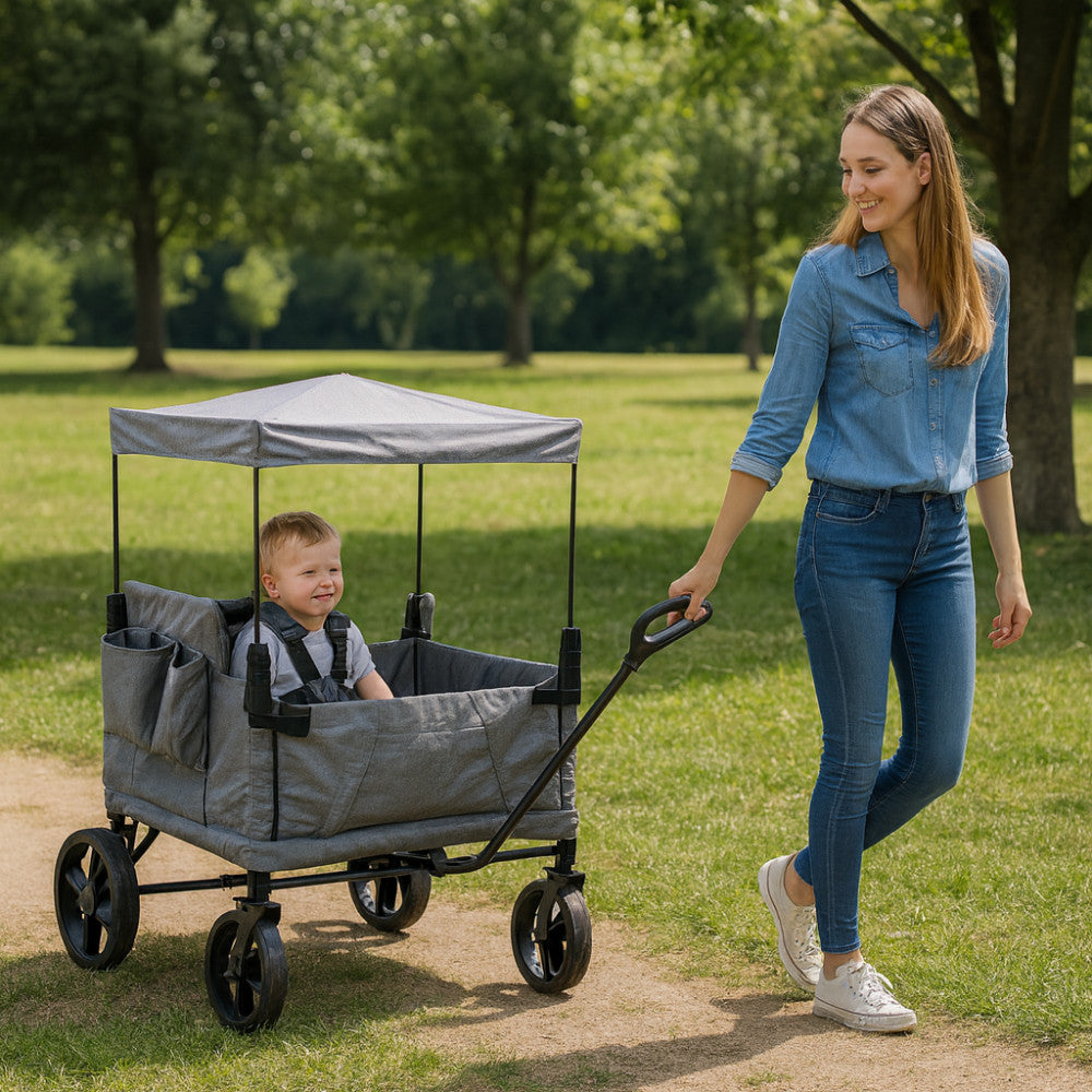 Donna che traina il Carrello Caribben in un parco verde con un bambino seduto all'interno, evidenziando la versatilità.