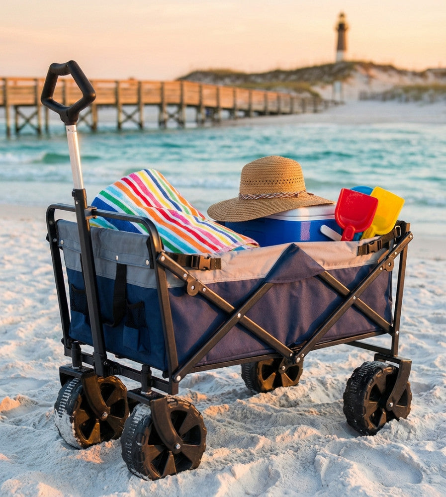 Carrello Pacific blu in acciaio, caricato con teli mare e accessori, posizionato sulla sabbia al tramonto.