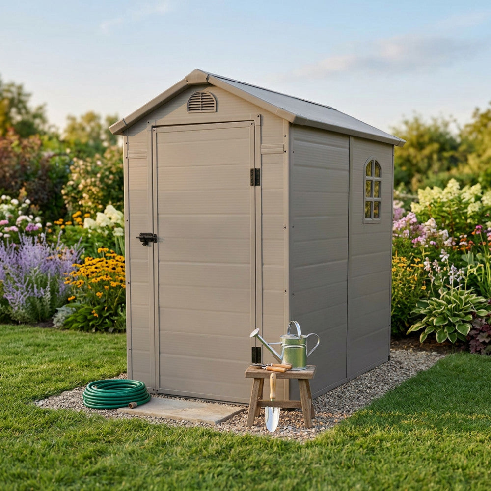 Vista frontale della casetta outdoor Home con porta chiusa, affiancata da attrezzi da giardinaggio in legno e un annaffiatoio in metallo zincato.