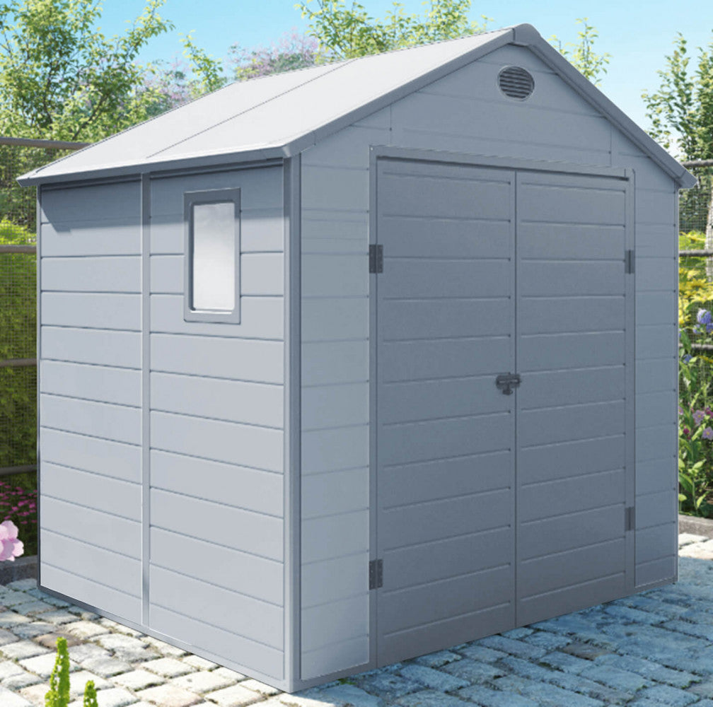 Casetta Home inserita in un cortile pavimentato con pietrini, illuminata dalla luce solare che esalta la texture a doghe orizzontali delle pareti.