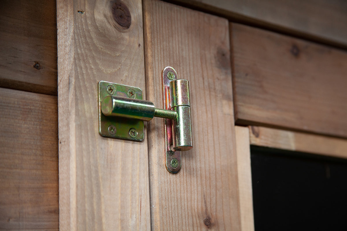 Dettaglio ravvicinato della robusta cerniera in metallo zincato sulla porta in legno di abete.