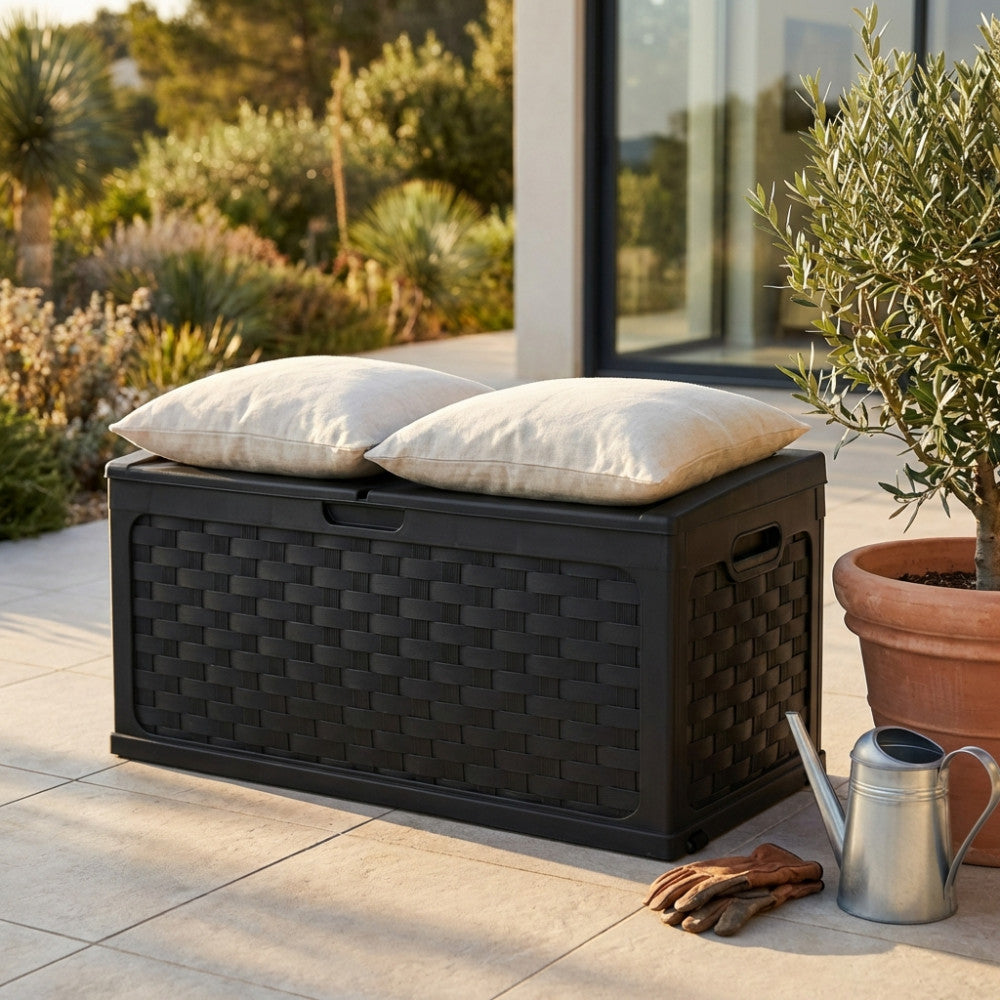 Cassapanca da esterno in plastica antracite effetto rattan, allestita su un patio soleggiato con due cuscini chiari sulla seduta.