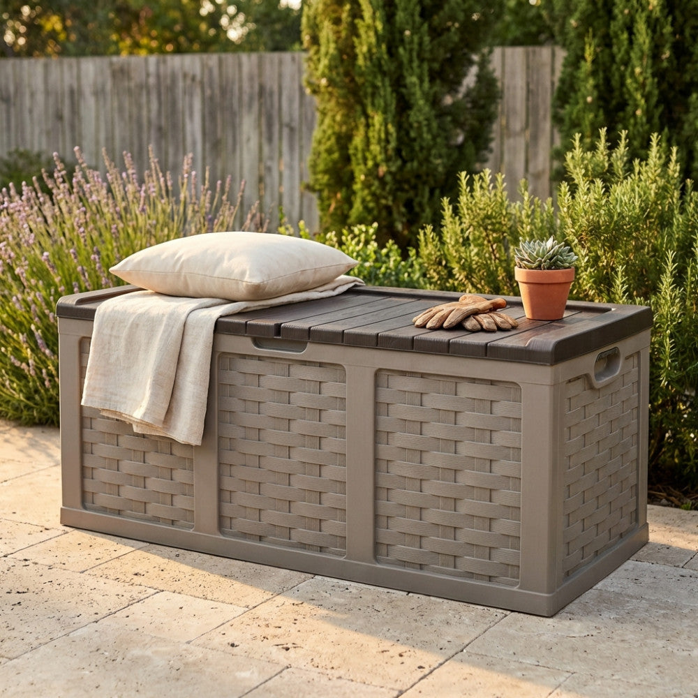 Cassapanca Rattan Style XXL marrone posizionata in un giardino soleggiato, decorata con un cuscino chiaro e attrezzi da giardinaggio.