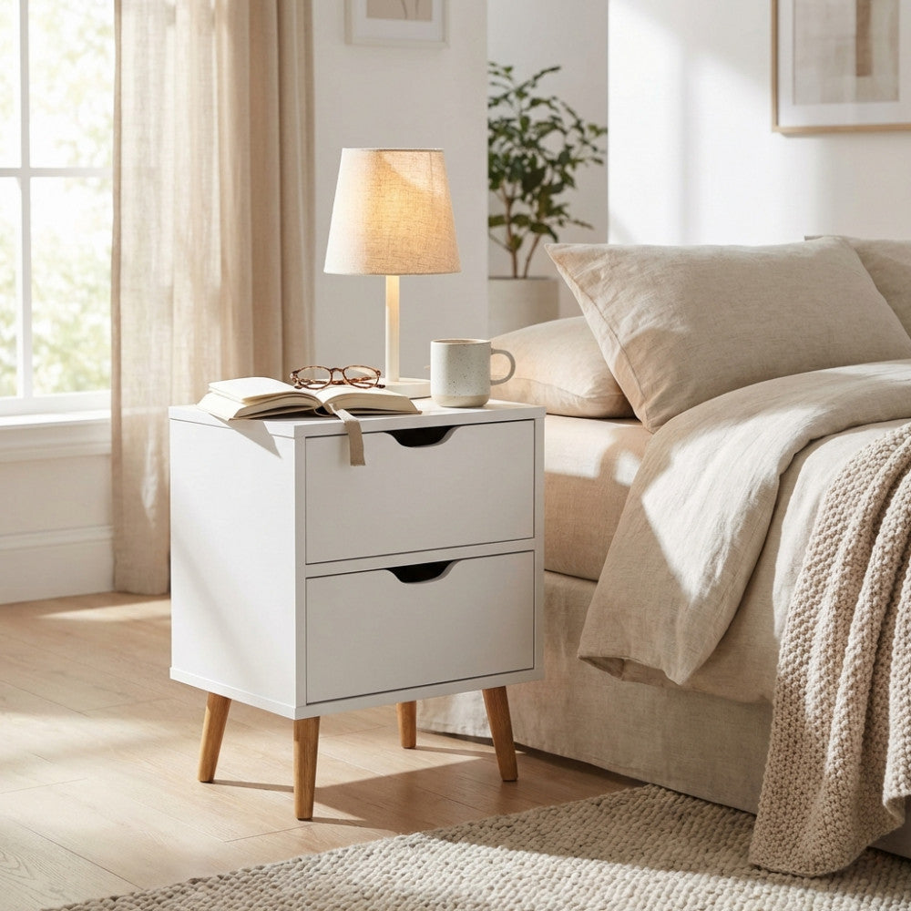 Comodino in legno bianco Amos ambientato in una camera da letto luminosa.