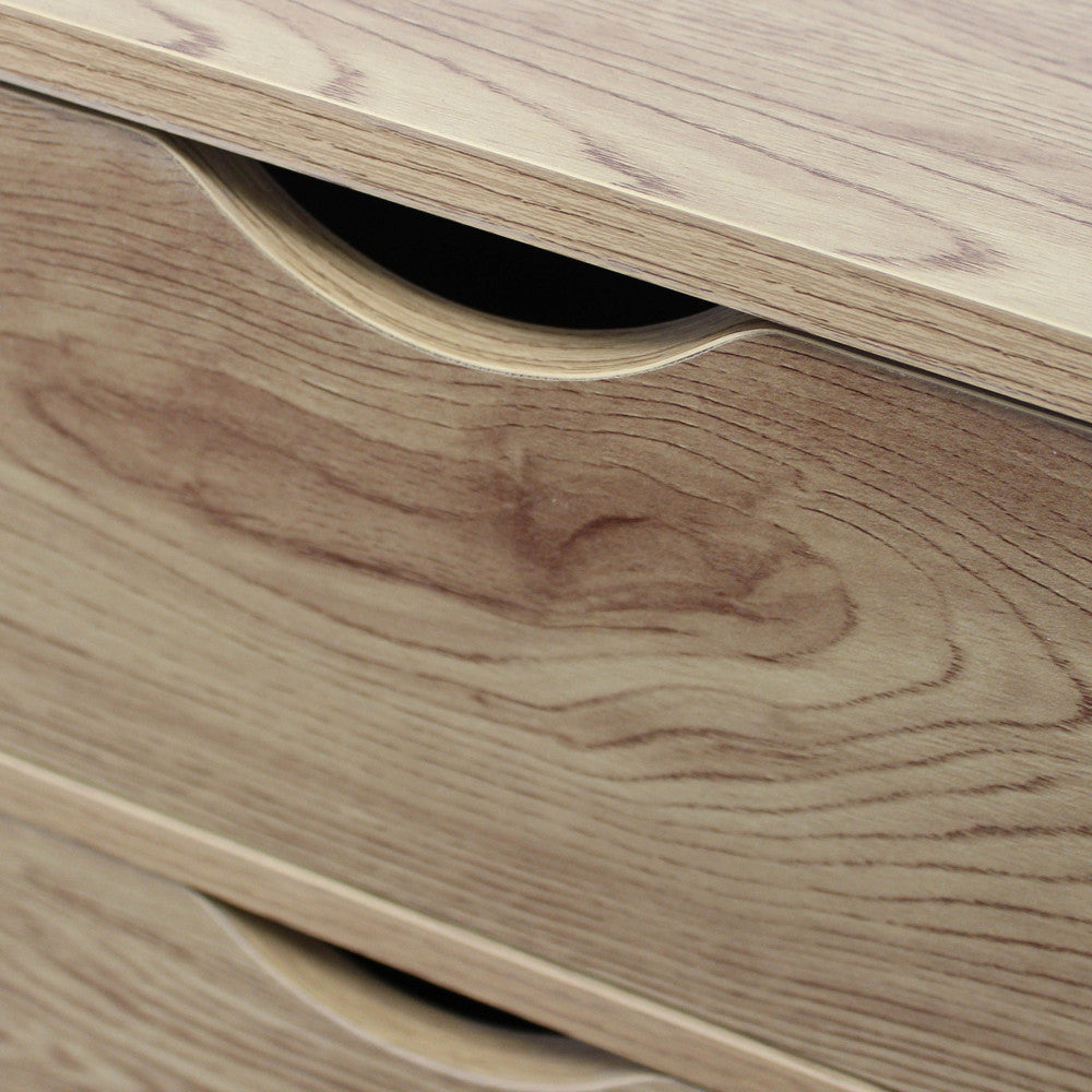 Dettaglio macro della maniglia a gola scavata nel legno marrone chiaro del cassetto superiore.