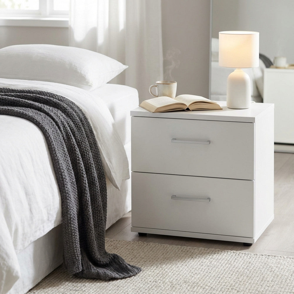 Comodino Ares bianco di fianco a un letto con lampada accesa, tazza e libro aperto.