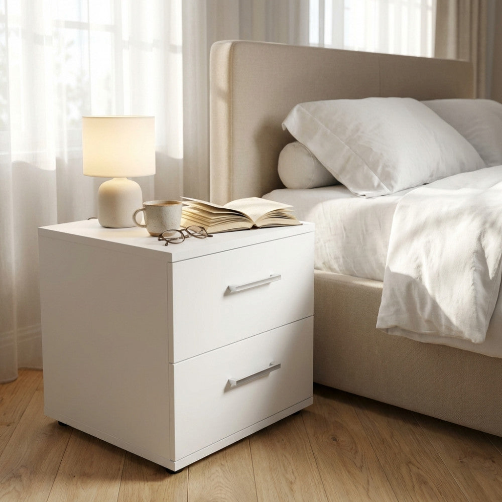 Comodino Ares bianco accanto a un letto imbottito beige, illuminato dalla luce naturale.