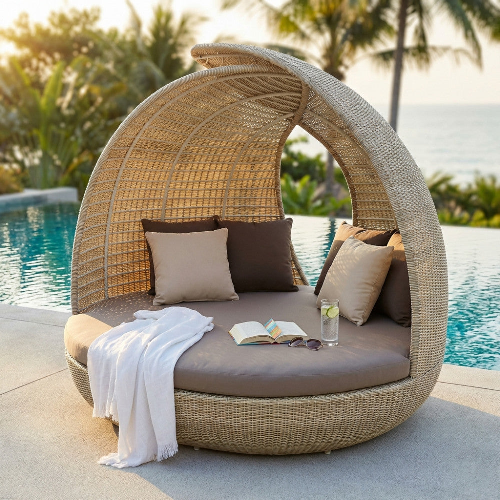 Conchiglione Palma in wicker marrone posizionato a bordo piscina con cuscini beige e marroni, asciugamano bianco e libro aperto.