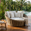 Divano lounge rotondo Conchiglione Quarter in rattan con morbidi cuscini bianchi, allestito su una terrazza in legno a bordo piscina.