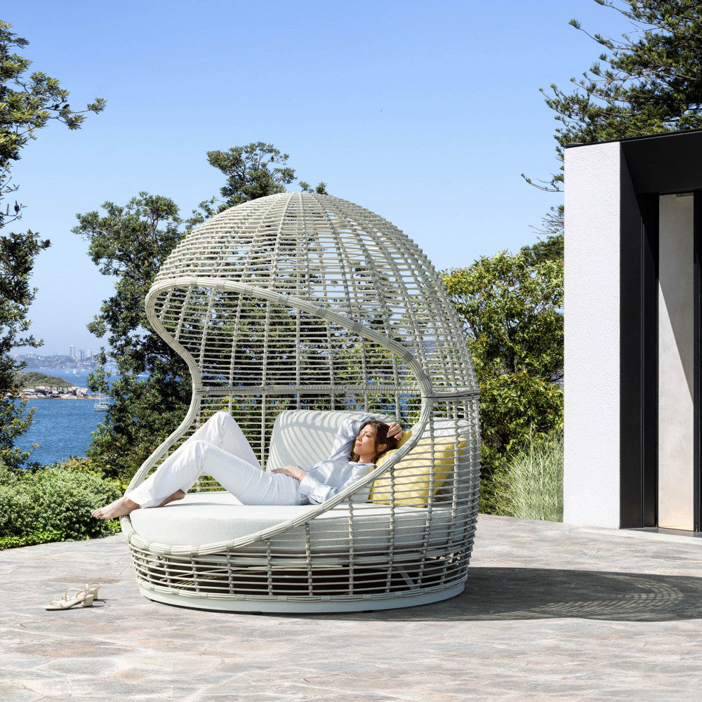 Donna che si rilassa sul daybed Ushuaia in wicker intrecciato vista mare.