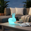 Lampada a forma di coniglietto luminoso azzurro su un tavolino da esterno in legno.
