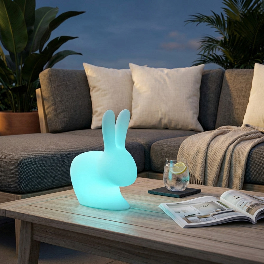 Lampada a forma di coniglietto luminoso azzurro su un tavolino da esterno in legno.