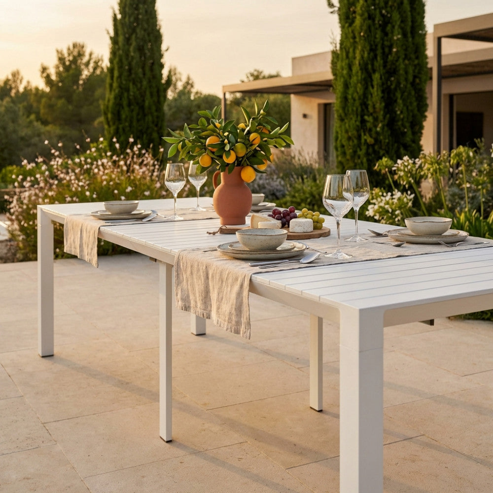 Dettaglio della superficie in alluminio bianco del tavolo da giardino esteso con mise en place elegante.