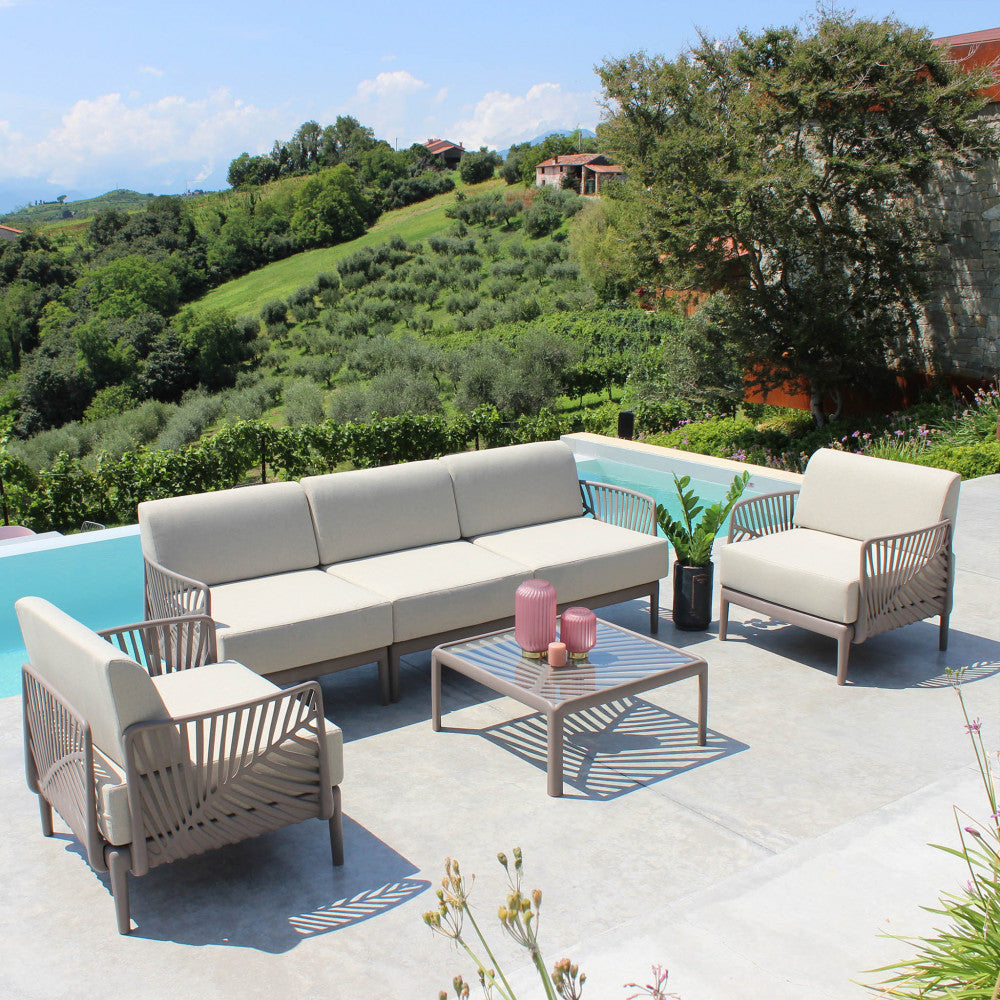 Salotto outdoor completo a bordo piscina, incorniciato dai braccioli taupe dal design scultoreo e cuscini sfoderabili.