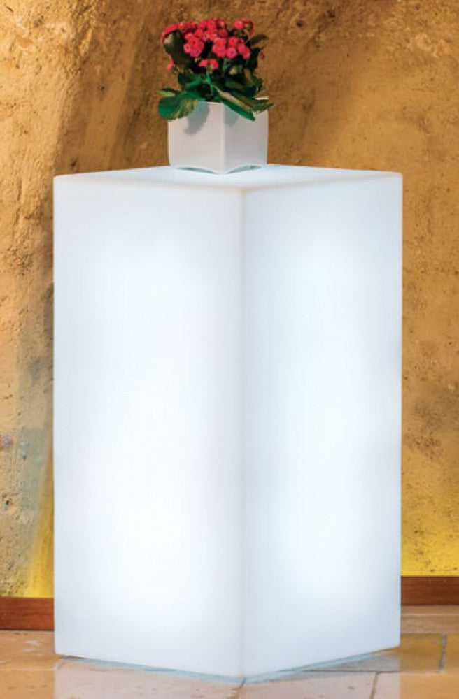 Lampada Cubo Indus utilizzata come piedistallo luminoso per una pianta in un ambiente rustico.
