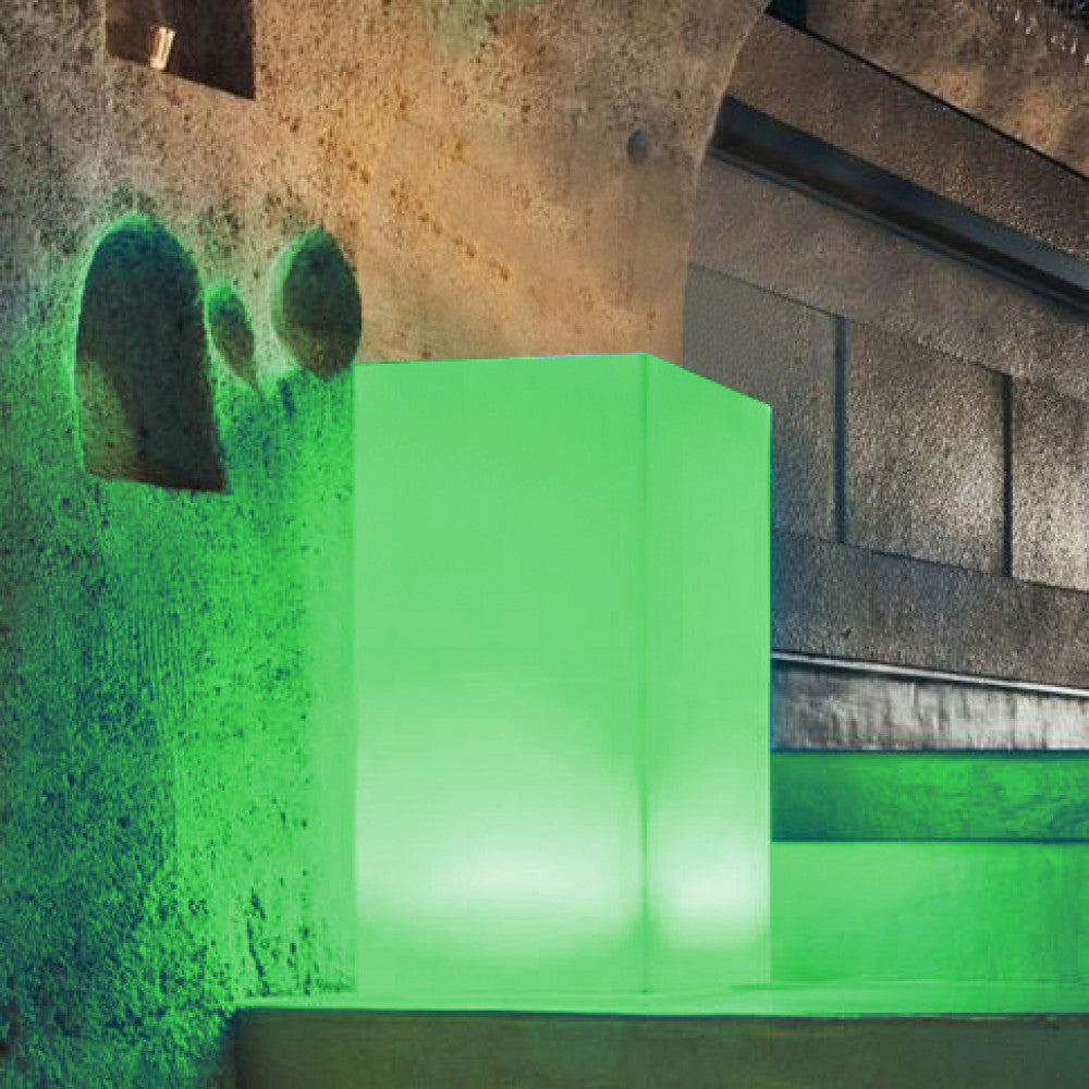 Lampada da terra Cubo Indus che diffonde luce verde smeraldo in una nicchia di pietra.