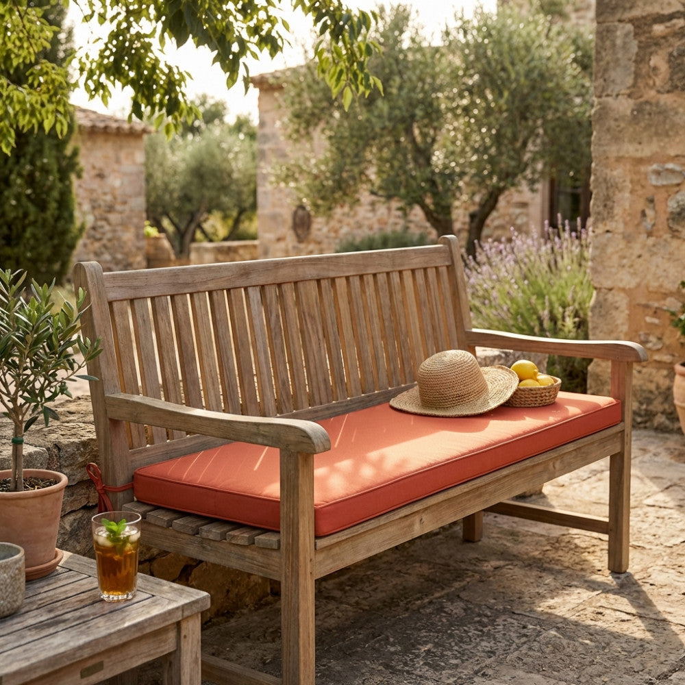 Vista ampia di una panchina da giardino in legno arricchita dal cuscino Real 110 arancione, inserita in un cortile rustico ed elegante circondato da ulivi e vegetazione mediterranea.