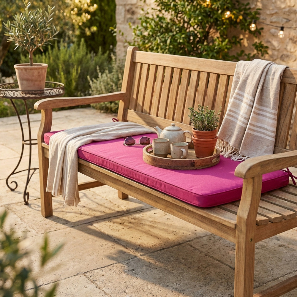 Panca da giardino in teak arricchita dal cuscino Real 110 color magenta, decorata con un vassoio in legno e set da tè in ceramica.