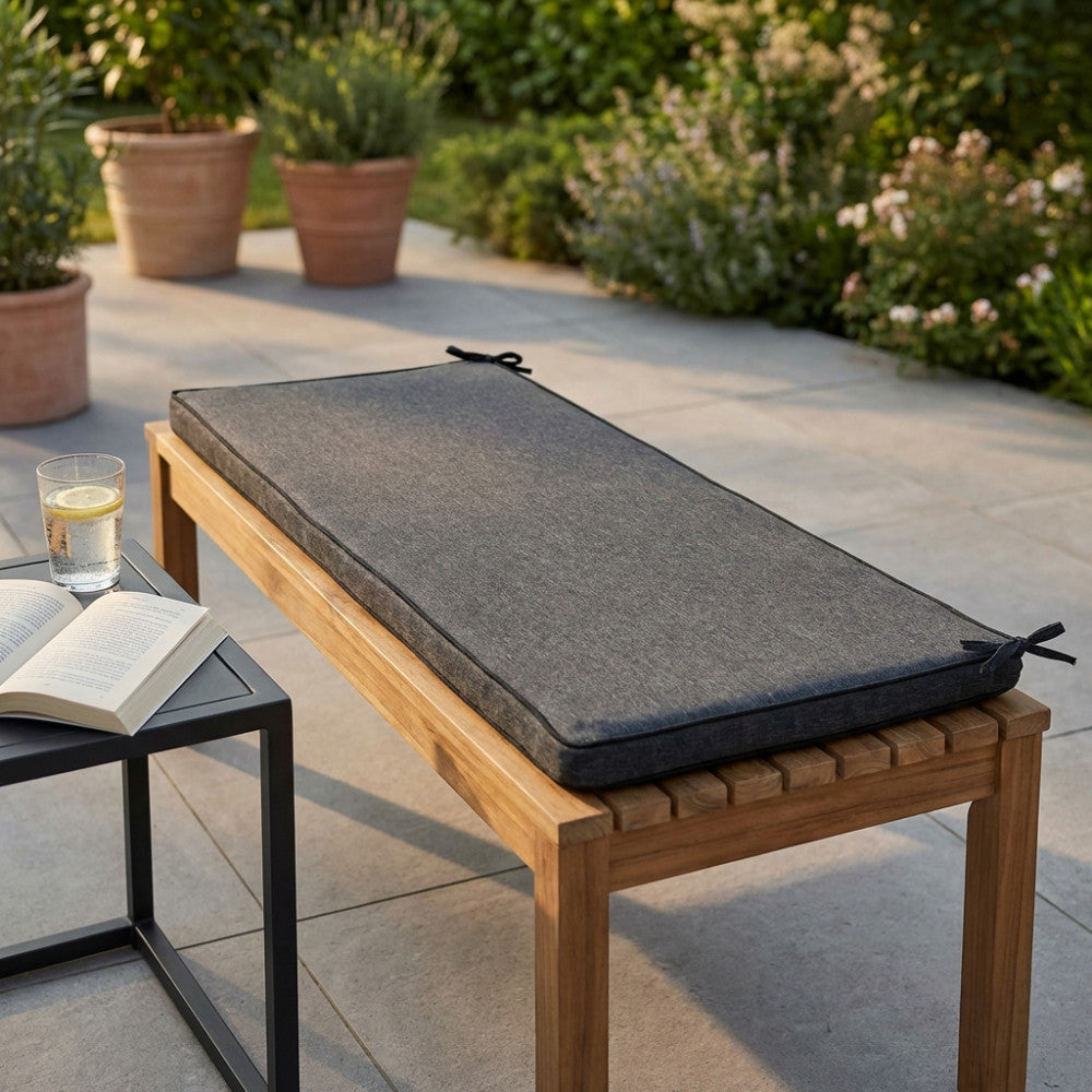 Cuscino per panca Real 110 in poliestere grigio scuro melange posizionato su una seduta in legno di teak in un giardino soleggiato.
