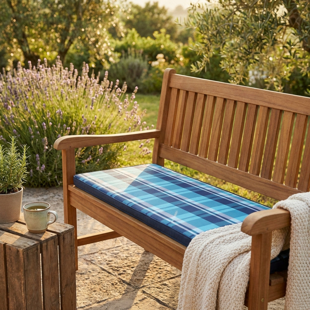 Vista angolare del Cuscino Real 110 Quadri Blu su una panchina in teak, circondato da piante di lavanda e vegetazione lussureggiante.