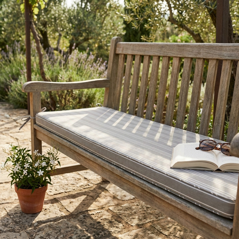 Dettaglio del Cuscino Real 110 Righe Tortora su una seduta in legno, con un libro aperto e occhiali da sole che invitano al relax.