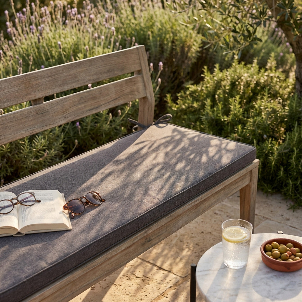 Dettaglio della texture in poliestere del cuscino Real 110 sulla seduta in legno, illuminato dalla luce naturale del giardino con libro e occhiali.