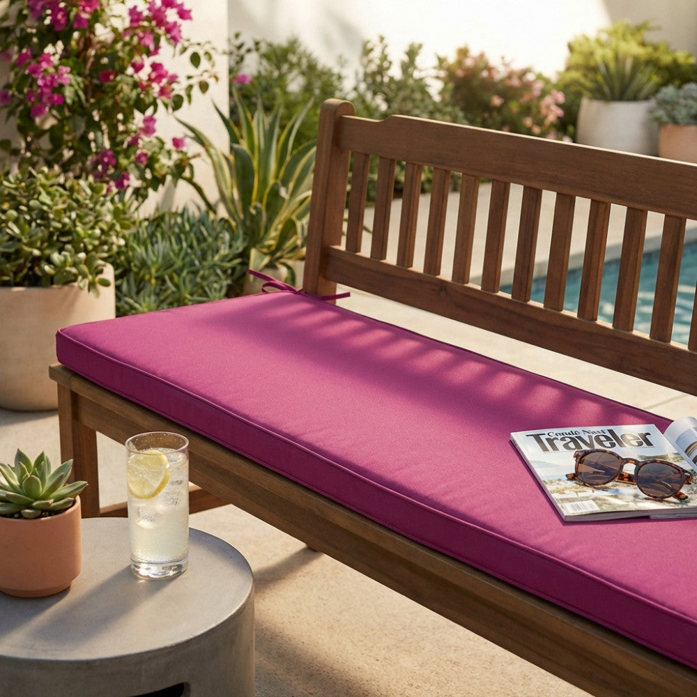 Cuscino magenta Real 150 posizionato su una panca in legno a bordo piscina, decorato con rivista e occhiali da sole.