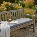 Cuscino Real 150 in poliestere grigio chiaro melange posizionato su una panca in legno in un rigoglioso giardino.