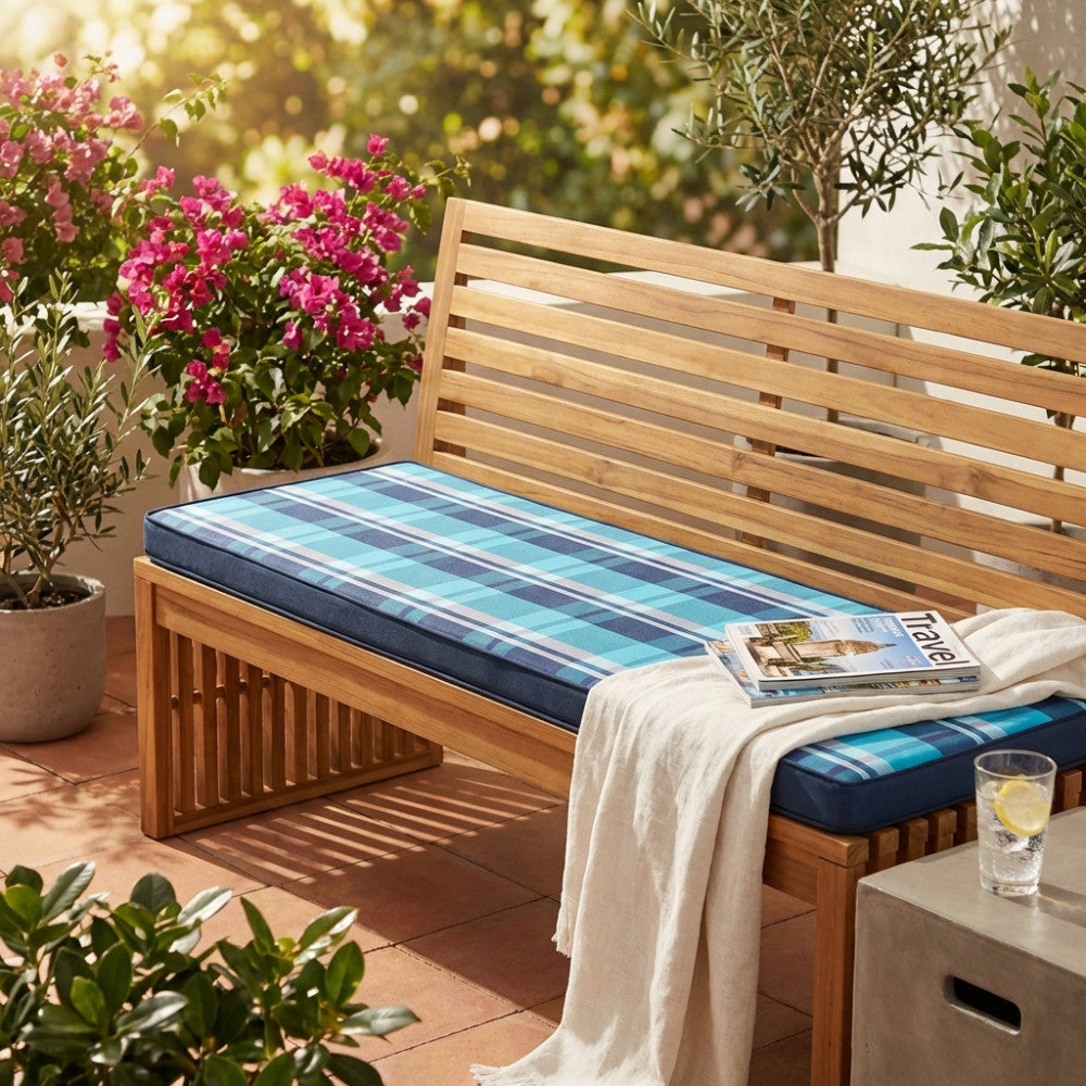 Cuscino Real 150 a quadri blu posizionato su una panca in legno in un patio soleggiato.