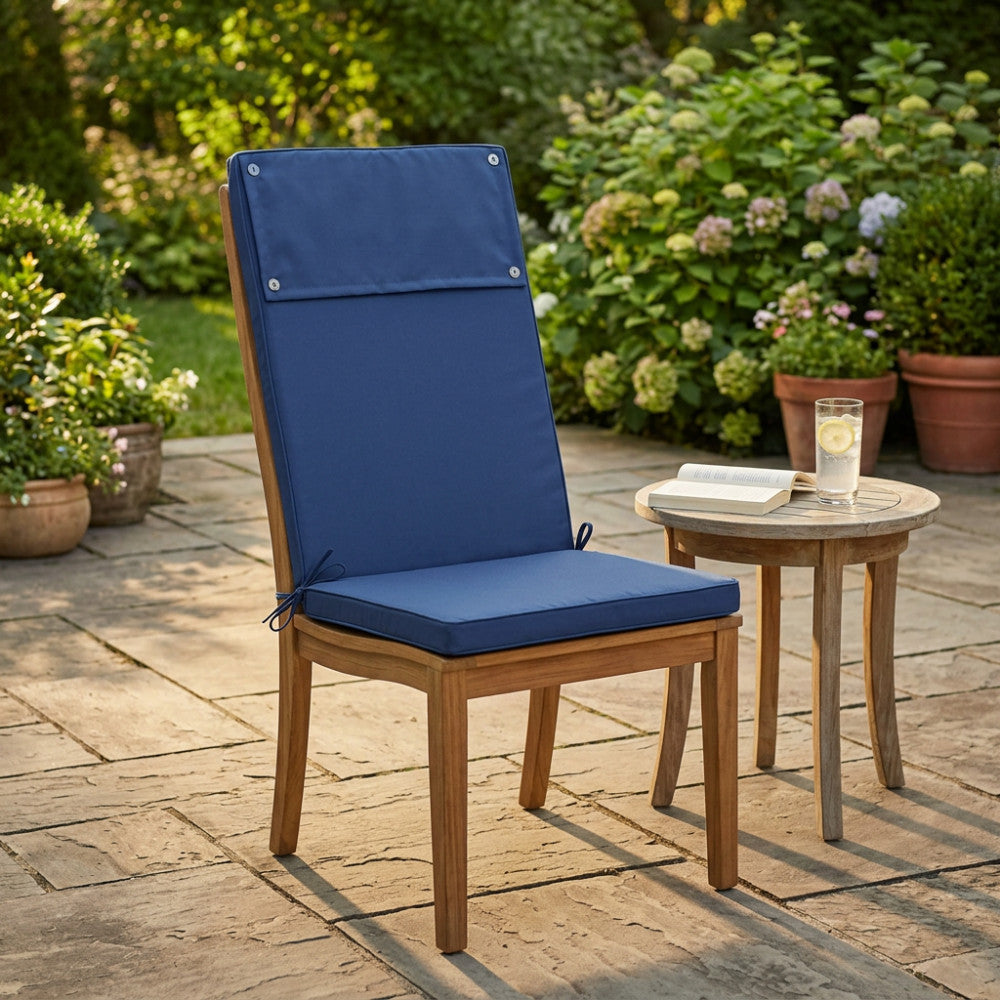 Cuscino Real Alto Blu Scuro posizionato su una sedia in legno di teak in un lussuoso giardino soleggiato.