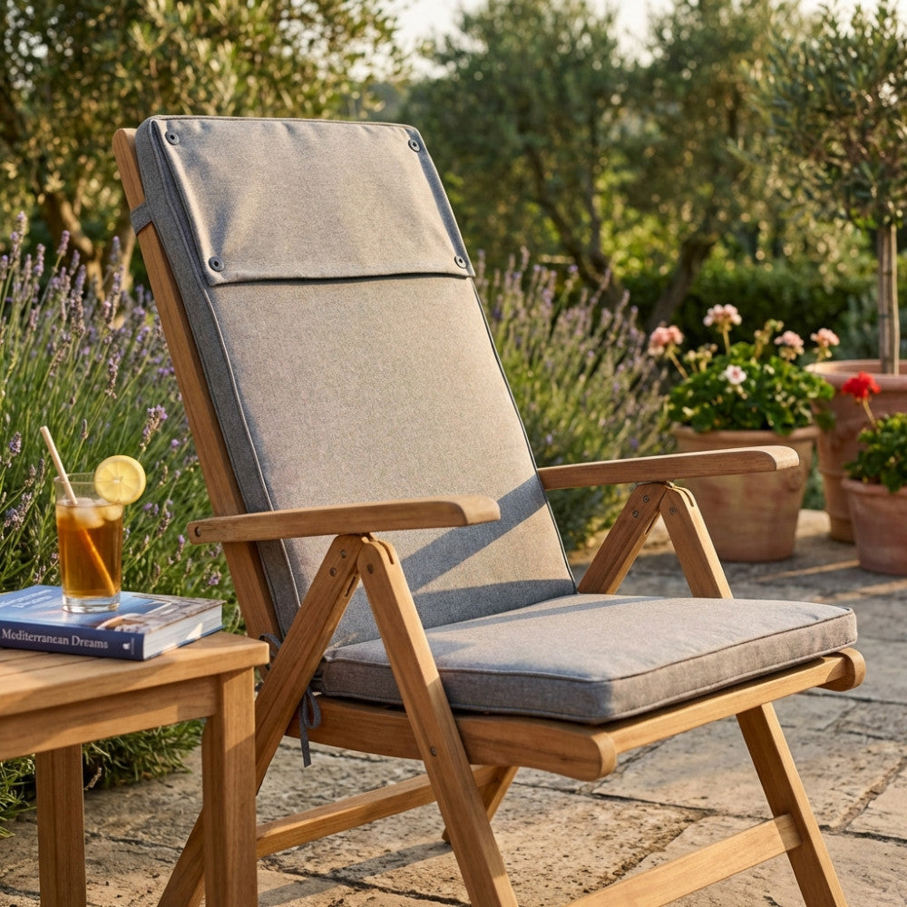 Cuscino Real Alto grigio chiaro melange posizionato su una sedia pieghevole in legno di teak in un giardino soleggiato.