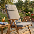 Cuscino Real Alto grigio chiaro melange posizionato su una sedia pieghevole in legno di teak in un giardino soleggiato.