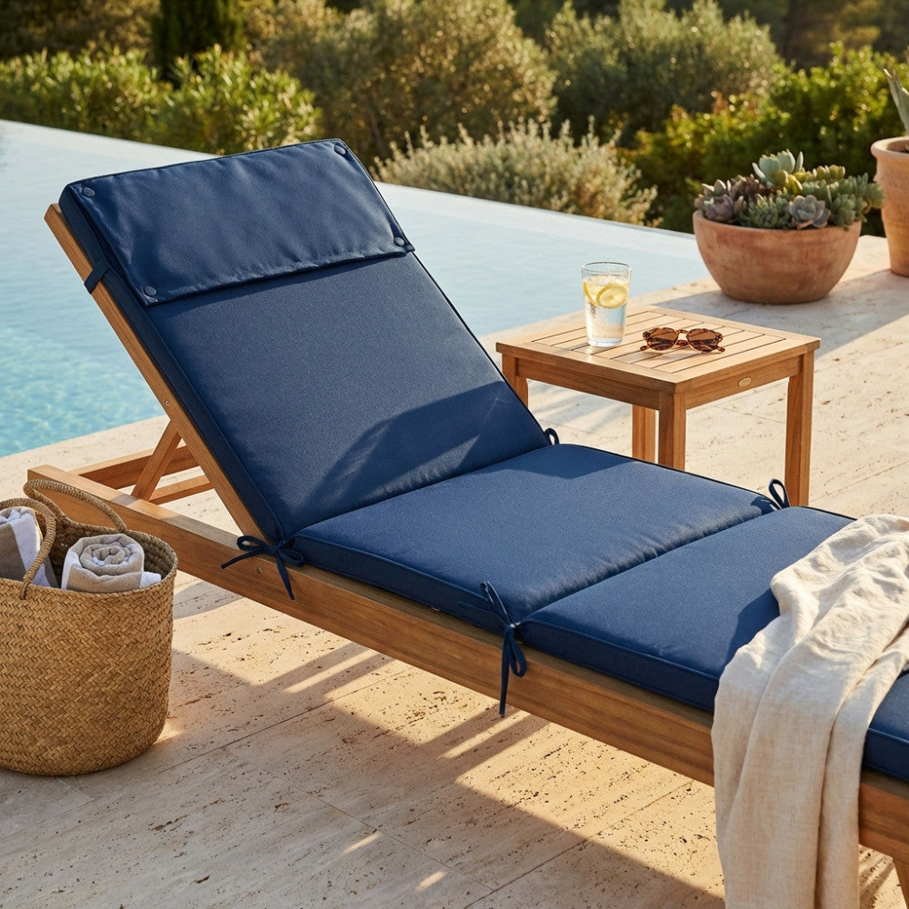 Dettaglio del cuscino blu scuro su un lettino in legno di teak, affiancato da un tavolino e accessori outdoor.