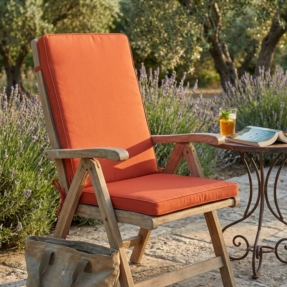 Cuscino Real Medio arancione posizionato su una sedia in legno in un rigoglioso giardino con lavanda.