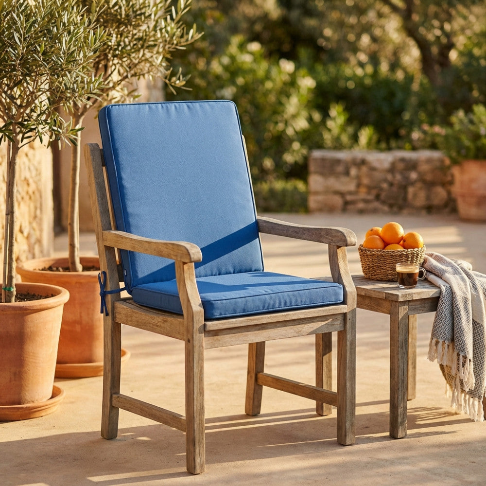 Cuscino Real Medio Blu Scuro su una sedia in legno, affiancato da un tavolino con un cesto di arance e una tazza di caffè, in un patio elegante.
