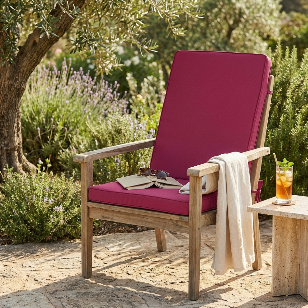 Cuscino Real Medio color magenta posizionato su una poltrona in legno in un elegante giardino.
